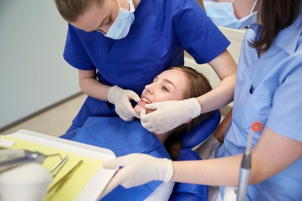 people, medicine, stomatology and teeth care concept - happy female dentist with assistant checking patient girl dental occlusion teeth at dental clinic office